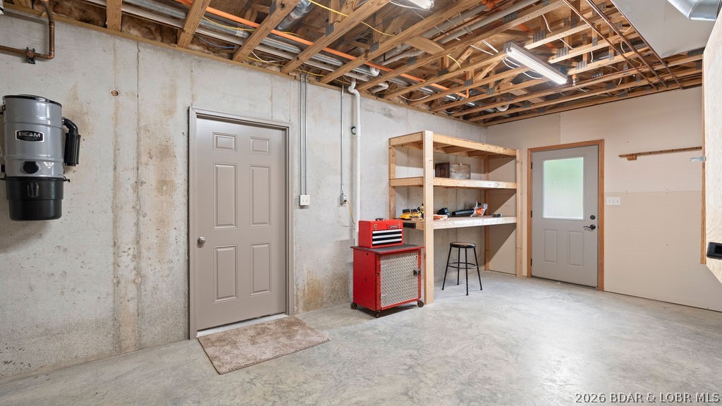 Basement workshop with exposed joists, wooden shelving, and a red tool cabinet.