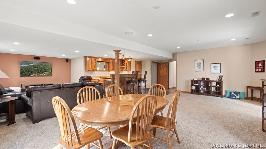 Open-plan living and dining area with a wooden table, leather sectional, and wood-finished bar.