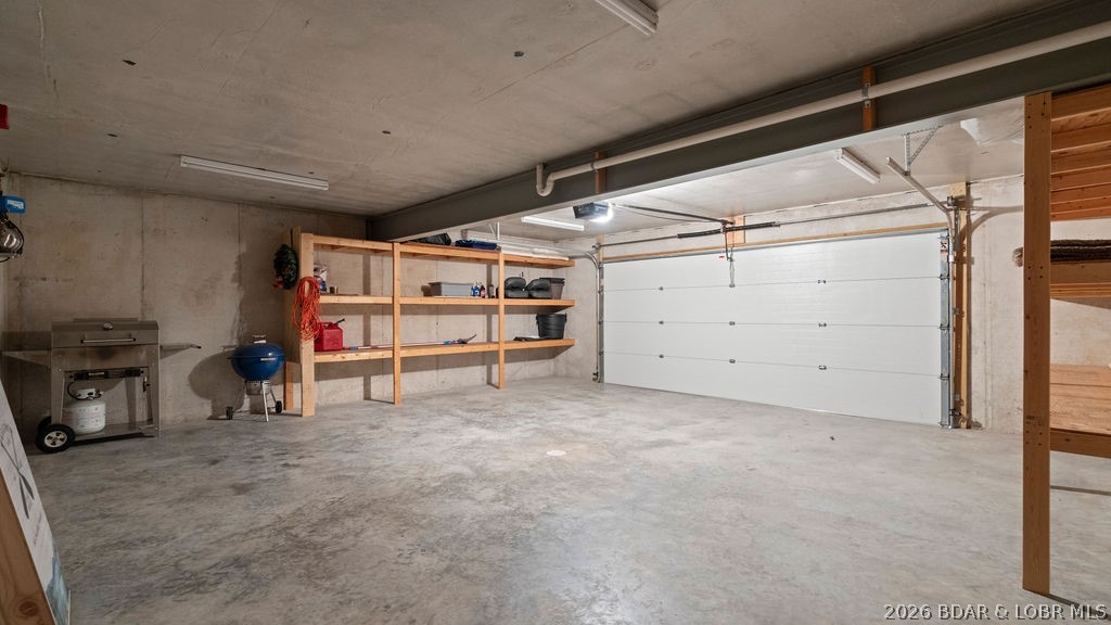 Spacious concrete garage with a white overhead door, wooden storage shelves, and two grills.