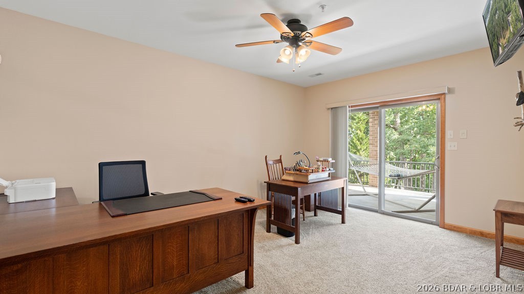 Furnished home office with wooden desks and sliding glass doors opening onto a tree-lined deck.