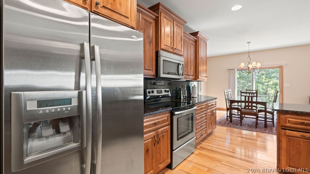 Kitchen with stainless steel appliances, warm wood cabinets, and a dining table beside a large window.