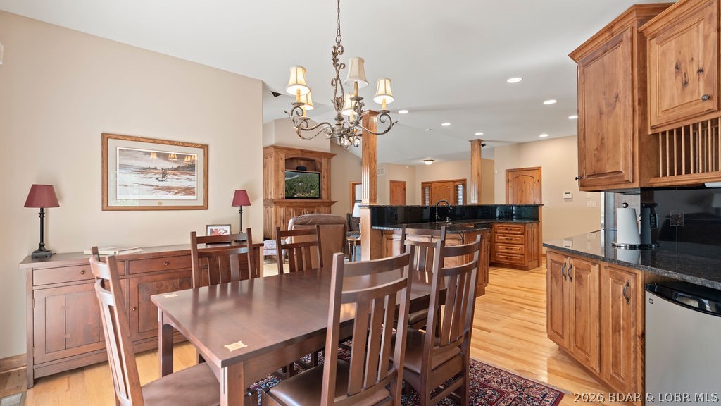Dining area with a large wooden table opening onto a kitchen with warm wood cabinets and black counters.