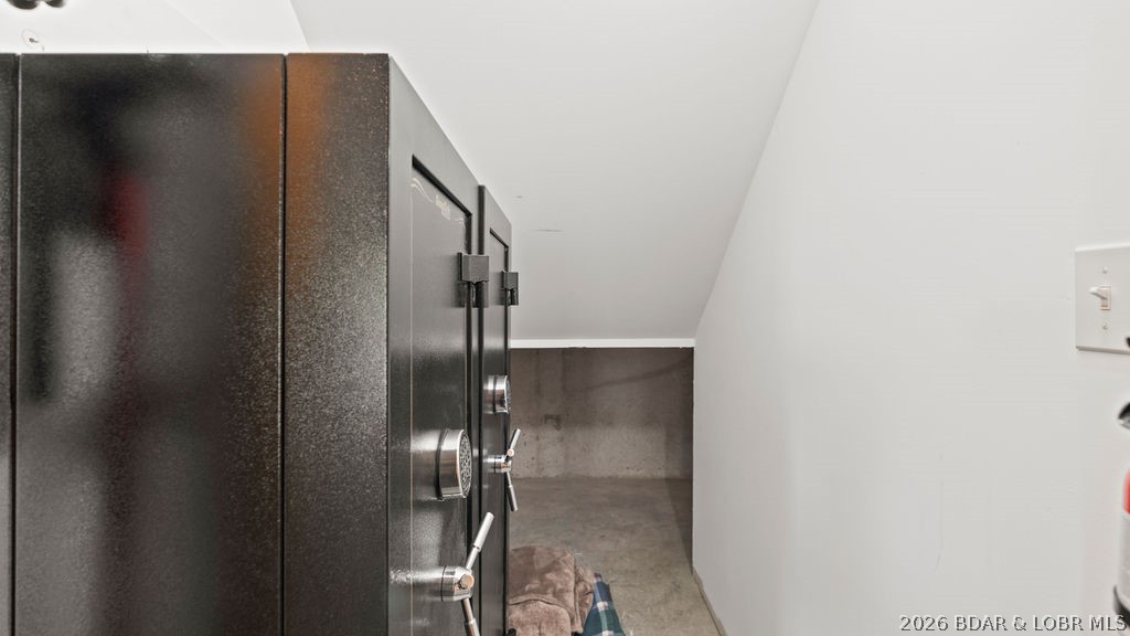 A large black combination safe stands in a narrow room with concrete flooring.