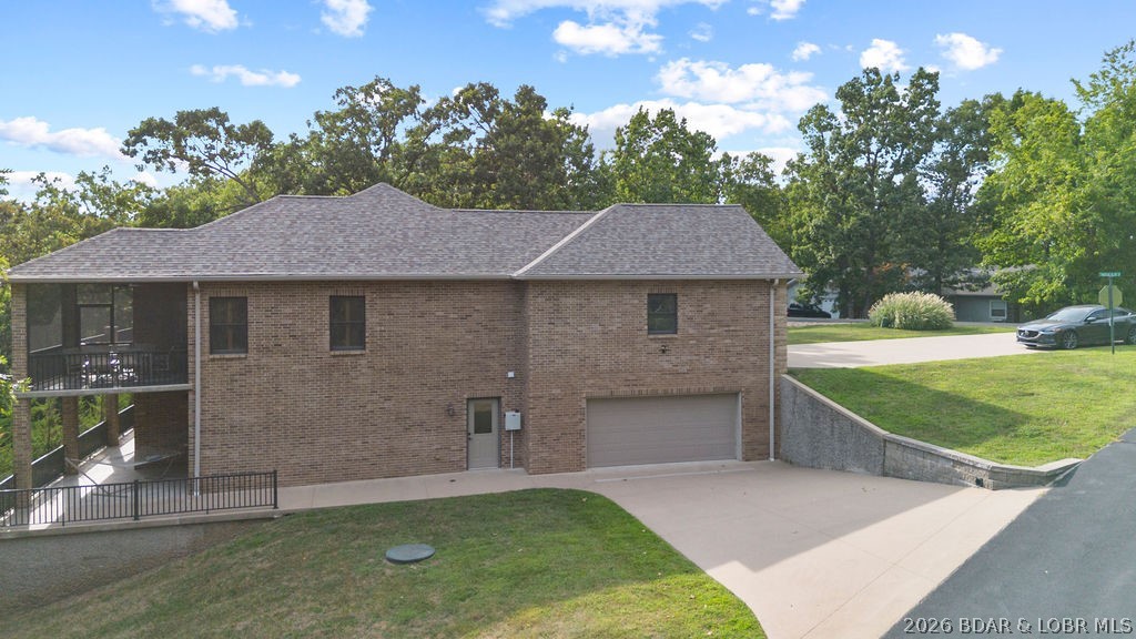 Brick home with an attached garage, covered balcony, and broad concrete driveway.