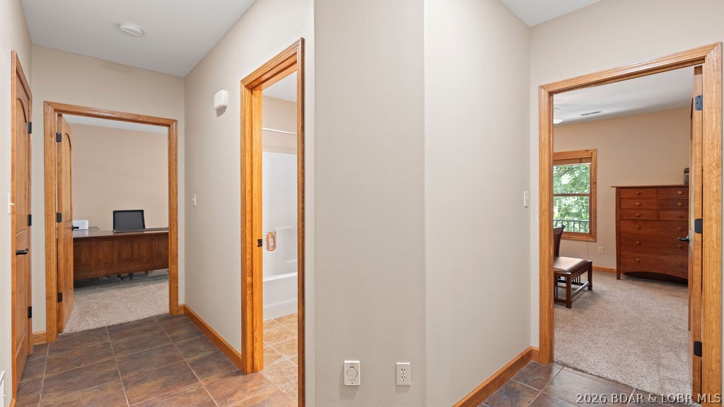 Hallway with wood-trimmed doorways to an office, bathroom, and bedroom with a dresser and bench.