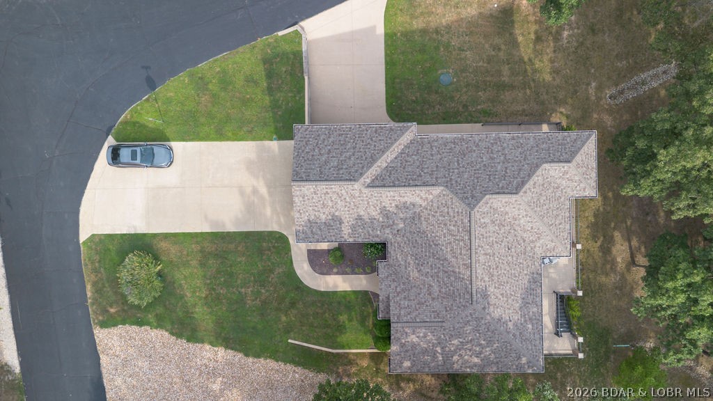 Aerial view of a house with a broad driveway, parked car, lawn, and curved street.