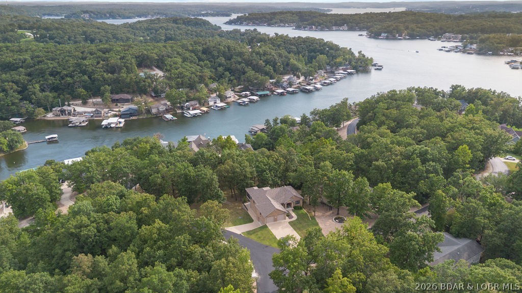 Aerial view of a wooded home near a lake inlet lined with homes and docks.