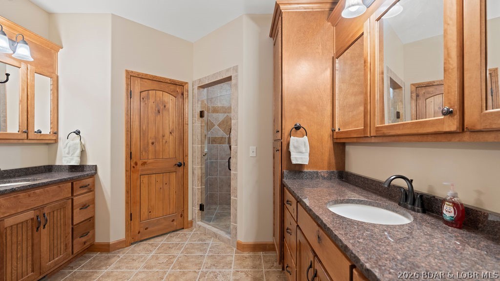Bathroom with wood cabinetry, granite vanity, tiled floor, and glass-enclosed shower.