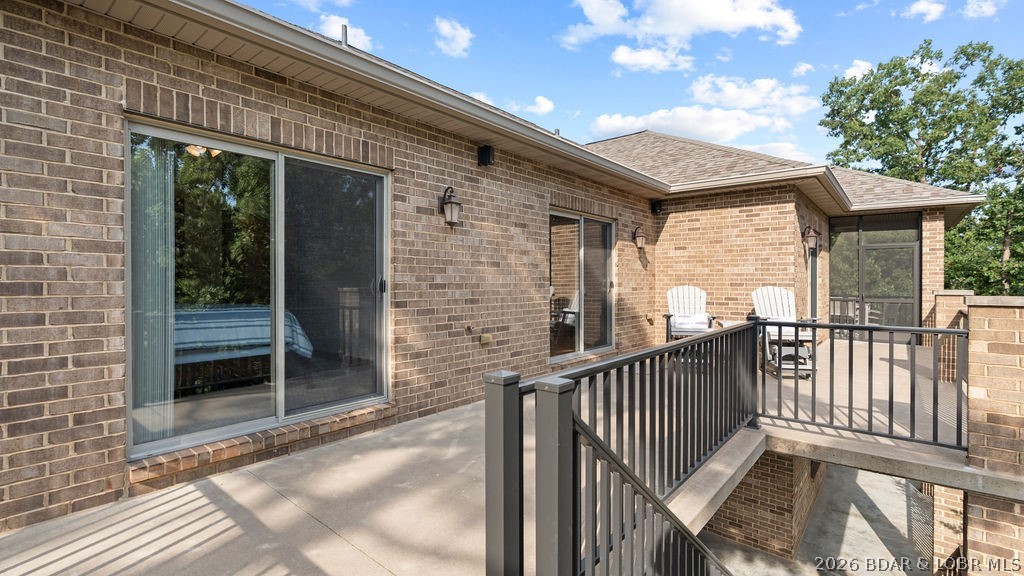 Raised patio with black railings and white Adirondack chairs beside a brick home.