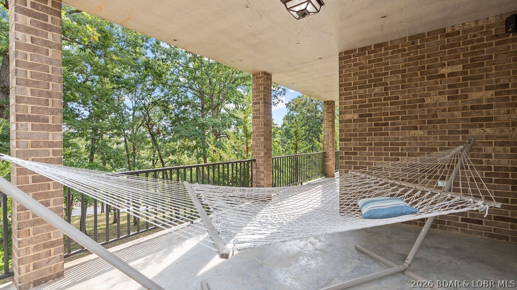 Covered brick porch with a white rope hammock overlooking leafy trees.