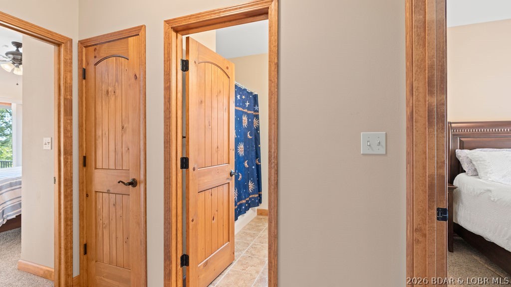 Hallway with warm wood trim and open doors leading to bedrooms and a tiled room.