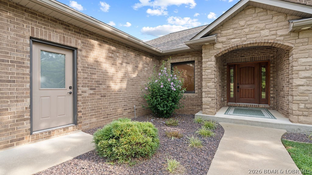 Brick-and-stone home entrance with a recessed wooden door, landscaped beds, and a curved walkway.