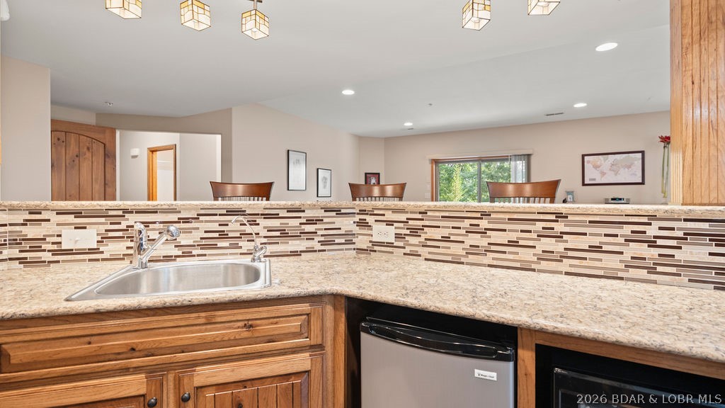 Kitchen with a granite counter, stainless-steel sink, wood cabinets, and raised mosaic-tile bar backsplash.