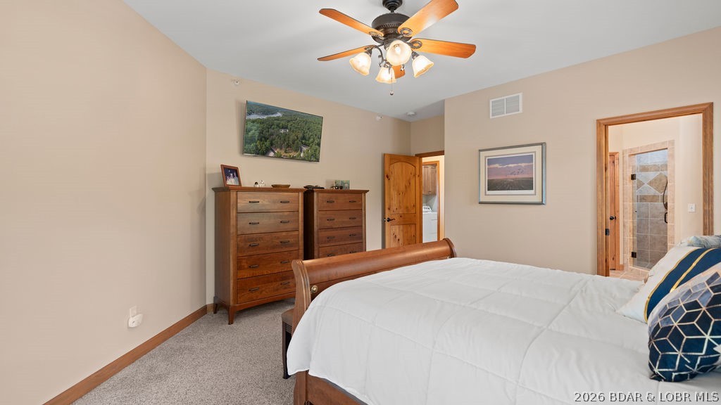Bedroom with a wooden bed, white quilt, matching dressers, and a doorway to a tiled bathroom.