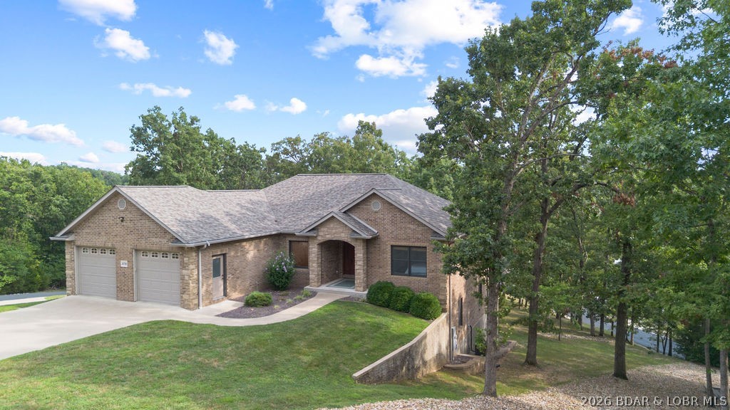 Brick home with a two-car garage and arched entry, set among mature trees beside the water.