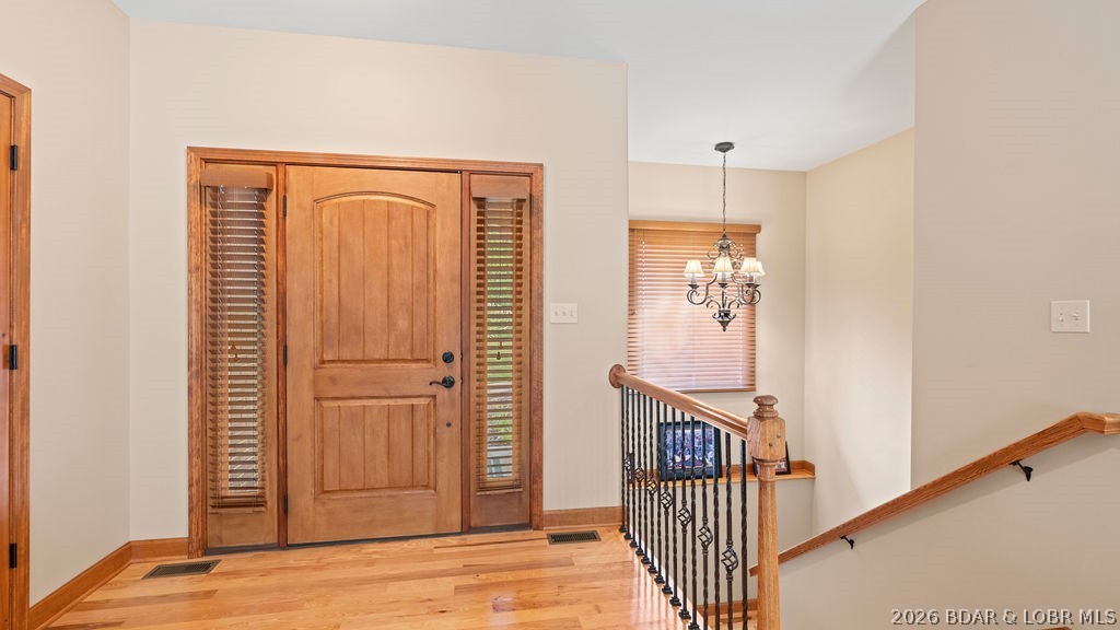 Entry foyer with a wood front door, hardwood floors, chandelier, and staircase railing.