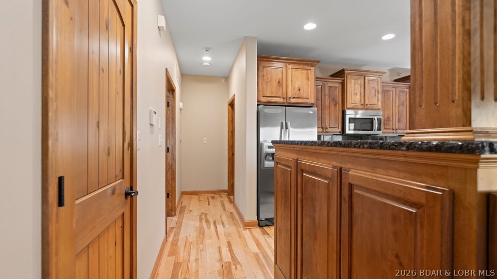 Kitchen with warm wood cabinets, dark granite counters, stainless steel appliances, and hardwood floors.