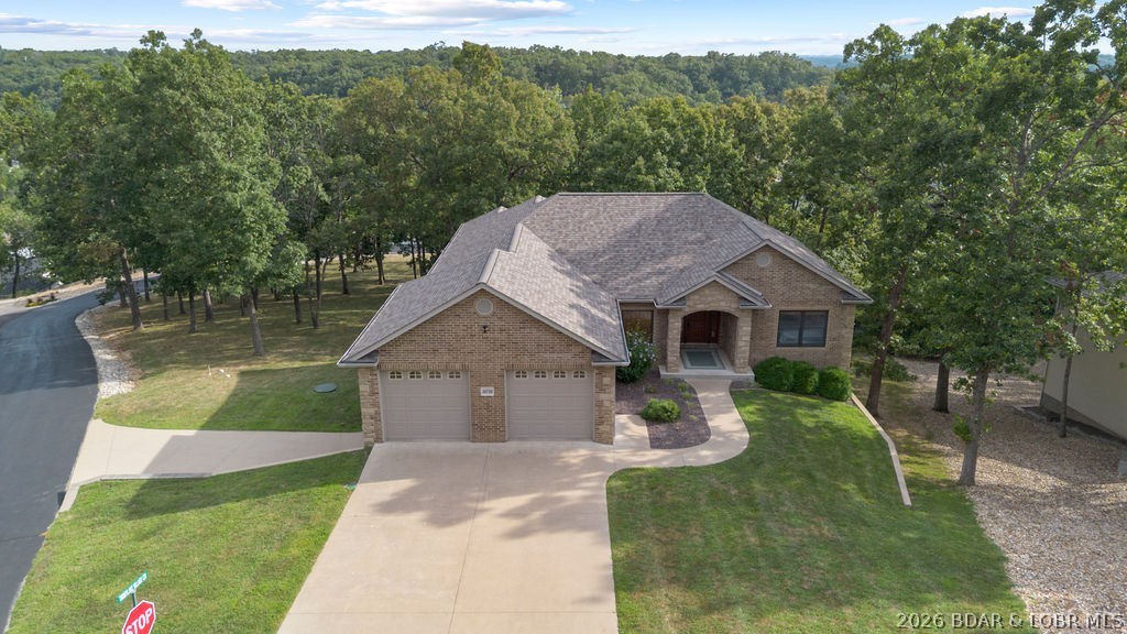 Aerial view of a brick home with a two-car garage and curved front walkway among mature trees.