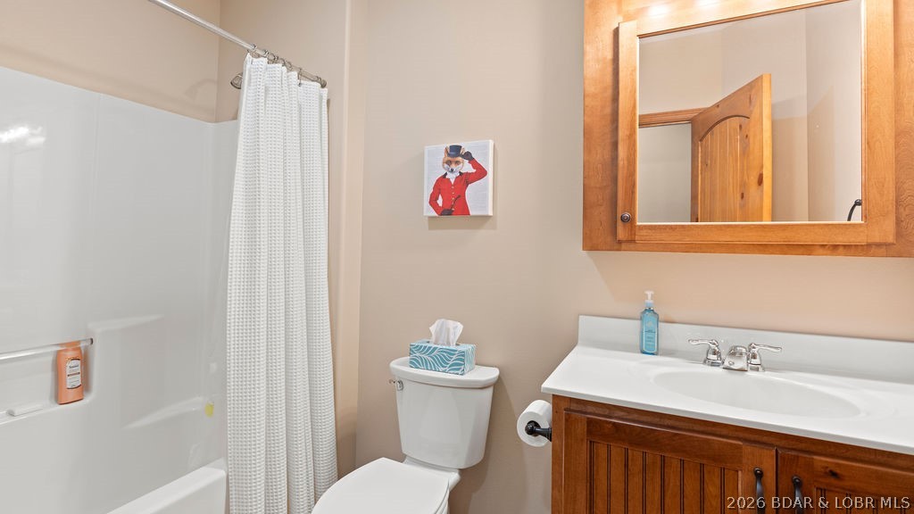 Bathroom with a white tub, shower curtain, toilet, and wood vanity with mirrored cabinet.