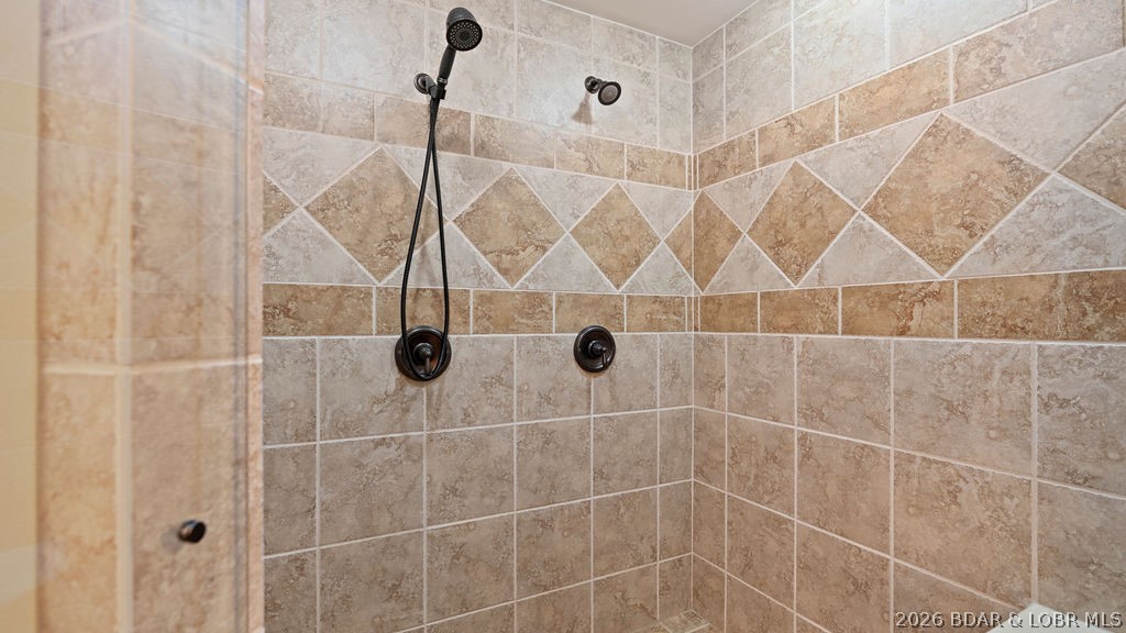 Tiled shower with a diamond-pattern accent band and dark bronze handheld showerhead.