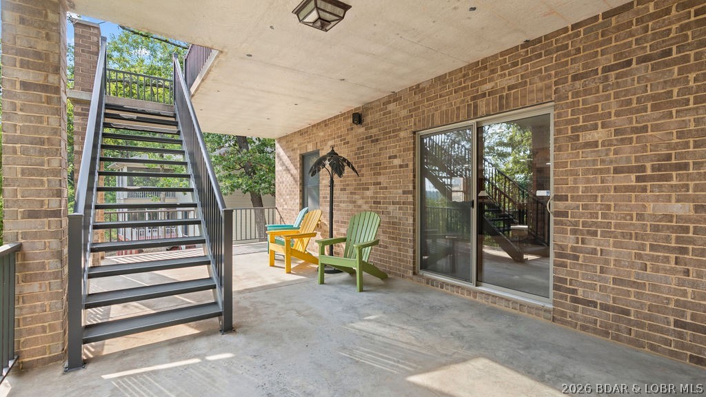 Covered brick patio with an exterior staircase and two colorful Adirondack chairs.