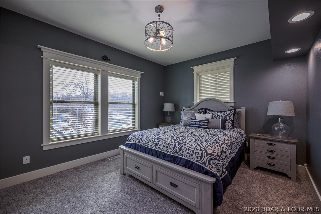 Bedroom with a gray bed, navy patterned bedding, and windows with white blinds.