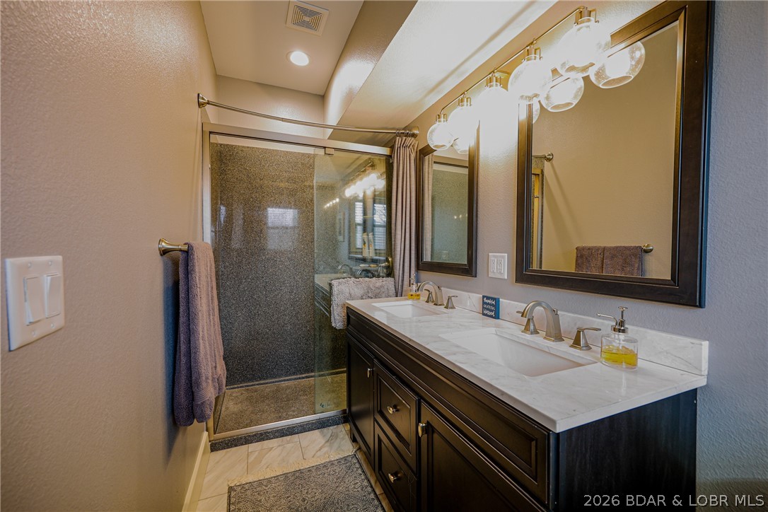 Bathroom with a glass shower and dark double vanity topped with white marble.