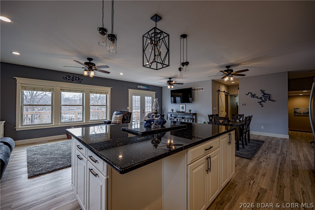 Open-plan kitchen with a large dark-granite island, pendant lights, and windows overlooking a deck.