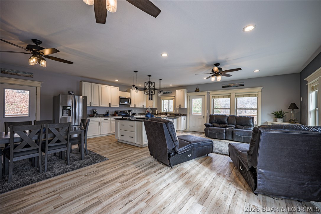 Open-concept living room and kitchen with dark leather seating, white cabinets, and wood-look floors.