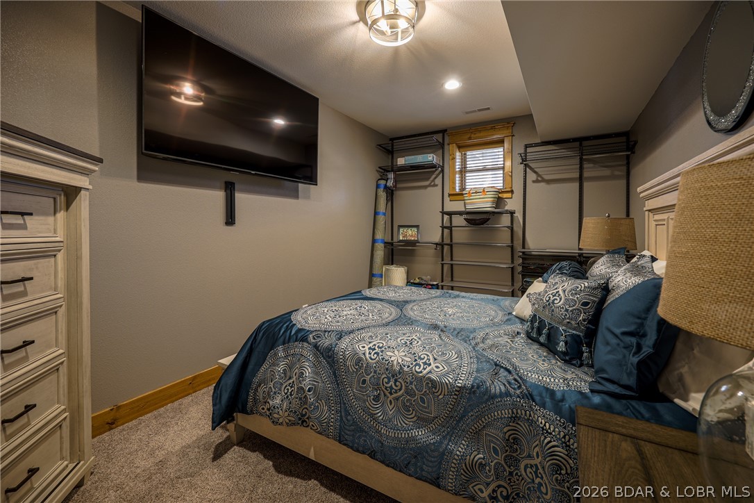 Bedroom with a blue patterned bedspread, wall-mounted TV, and open shelving.