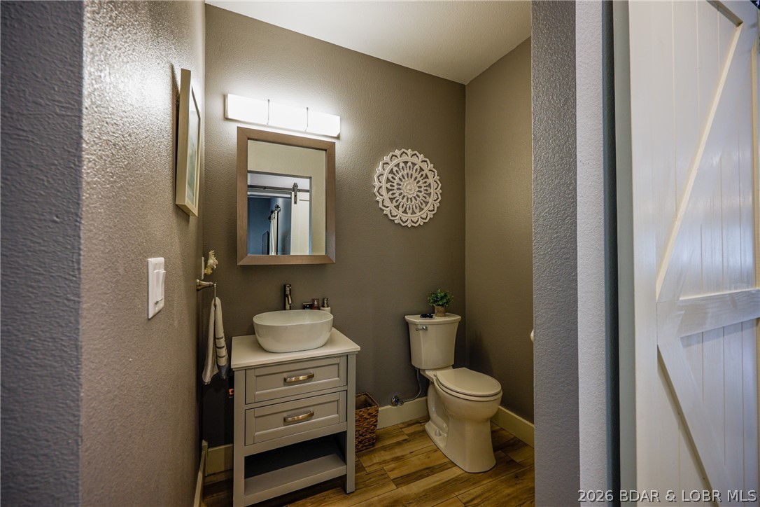 Bathroom with a vessel sink vanity, toilet, and wood-look plank flooring.