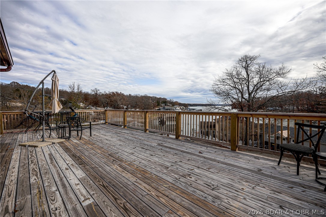 Wooden deck overlooking the lake, with patio chairs and leafless trees.