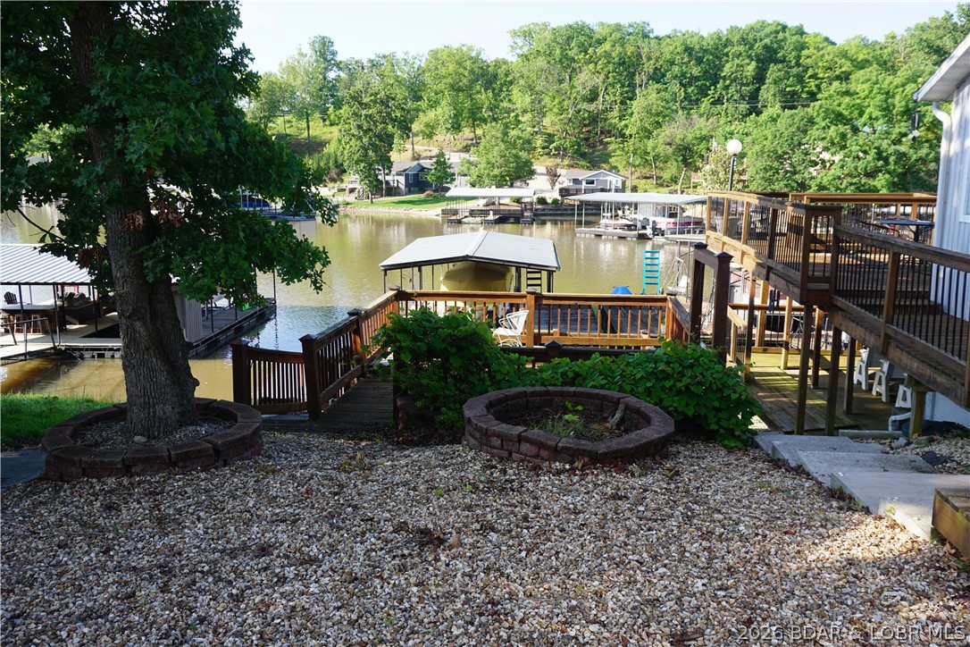 Lake cove and boat docks viewed from a gravel yard framed by a large tree and wooden decks.