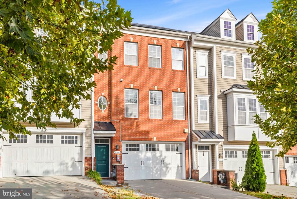 Townhouse with a red brick facade, white garage doors, and leafy trees.