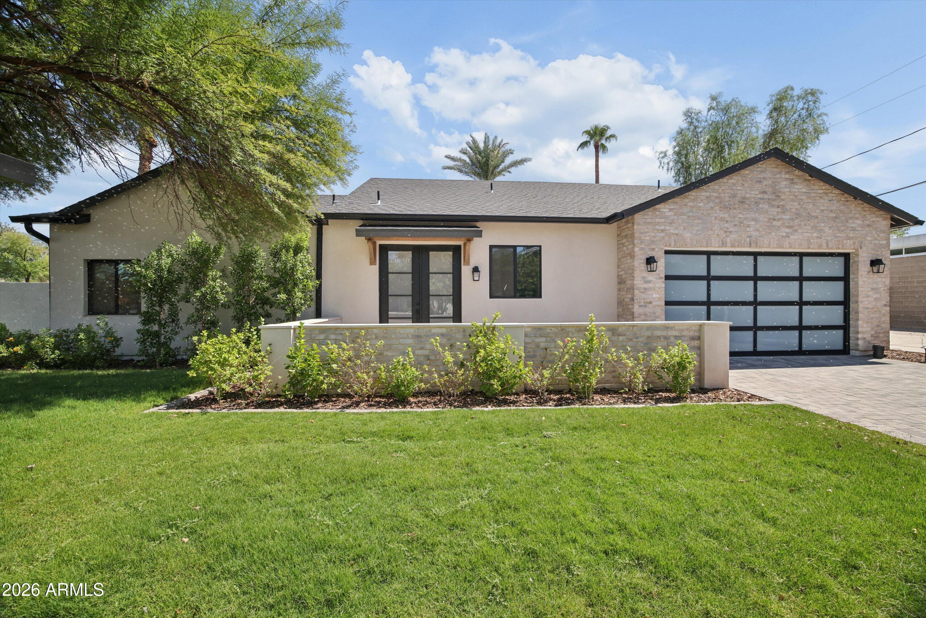 Modern stucco home with a brick garage surround, landscaped front wall, and broad green lawn.