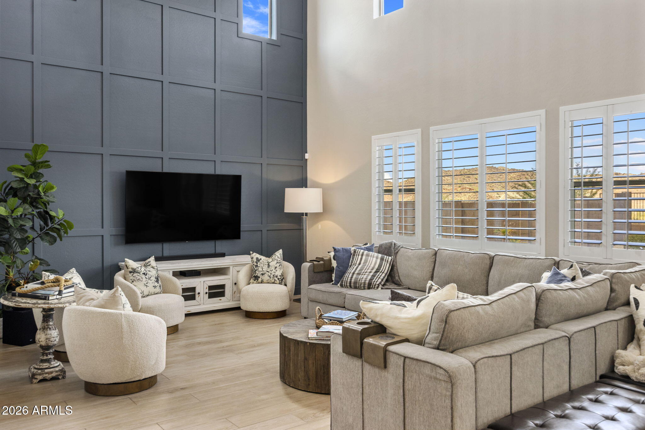 Living room with a tall paneled accent wall, sectional sofas, and windows overlooking desert hills.