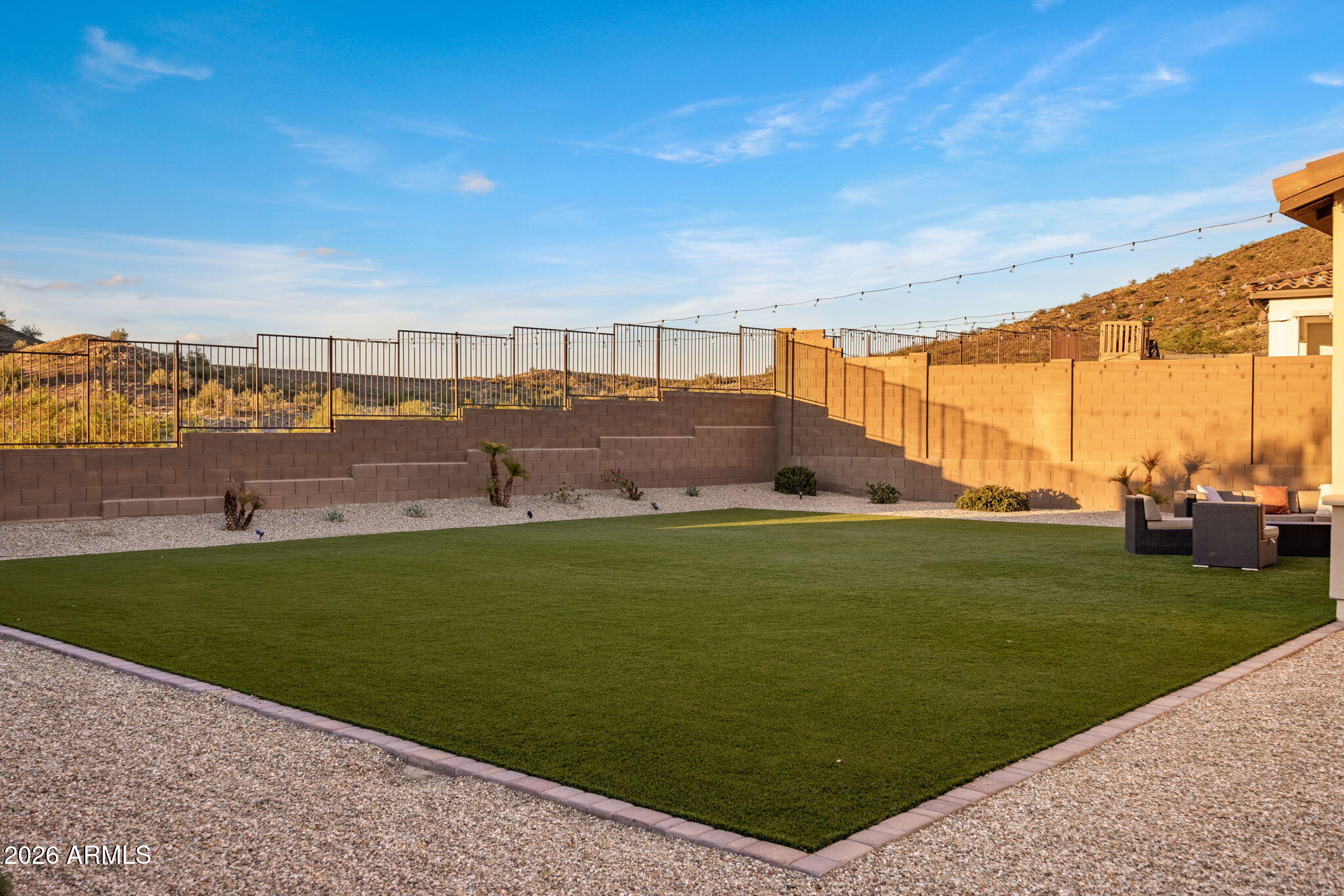 Backyard with a broad artificial-turf lawn, tiered retaining walls, and outdoor lounge seating.