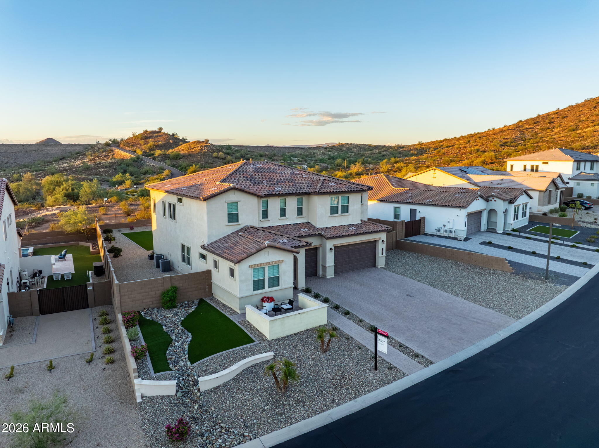 Aerial view of a two-story stucco home with a tiled roof, landscaped yard, and desert hills.
