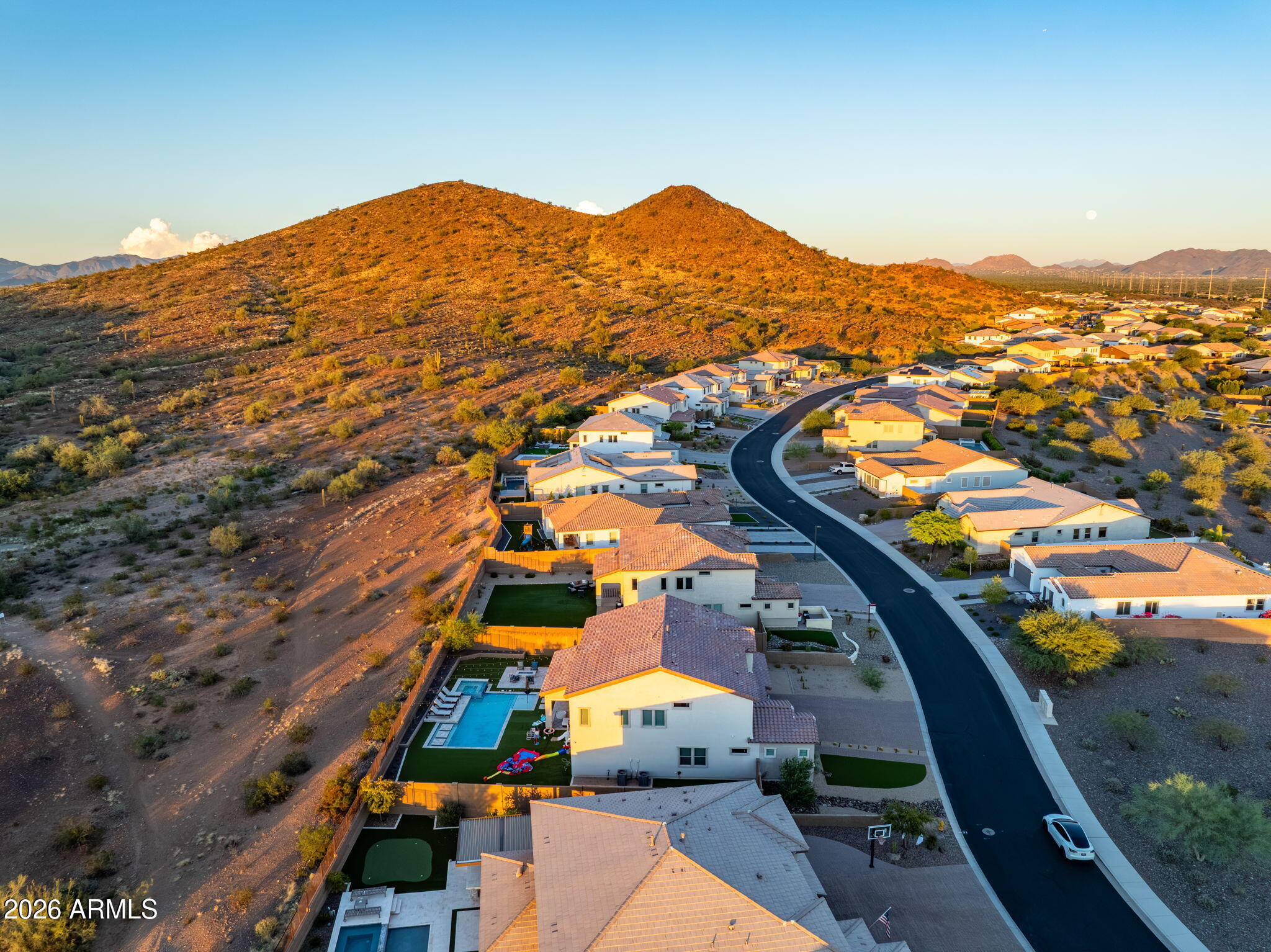 Aerial view of homes beside a desert hillside, with distant mountains and a backyard pool.