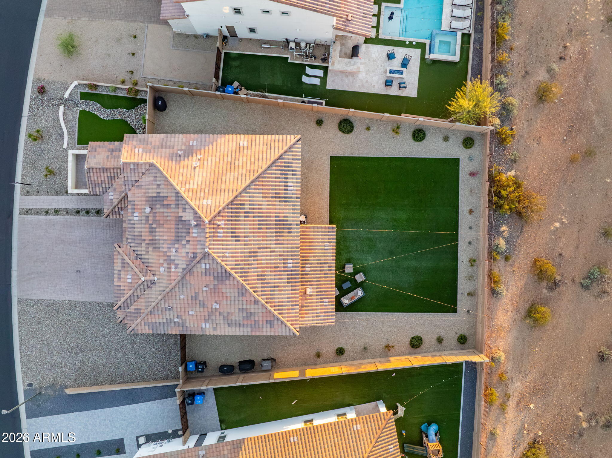 Aerial view of a backyard with a large turf lawn, gravel landscaping, patio seating, and a swimming pool.