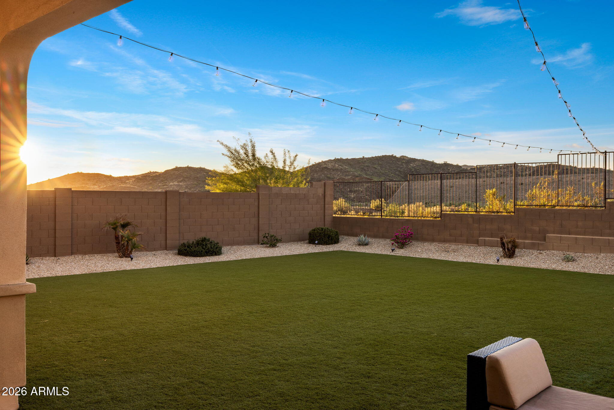 Backyard lawn with desert landscaping, overhead string lights, and mountain views at sunset.