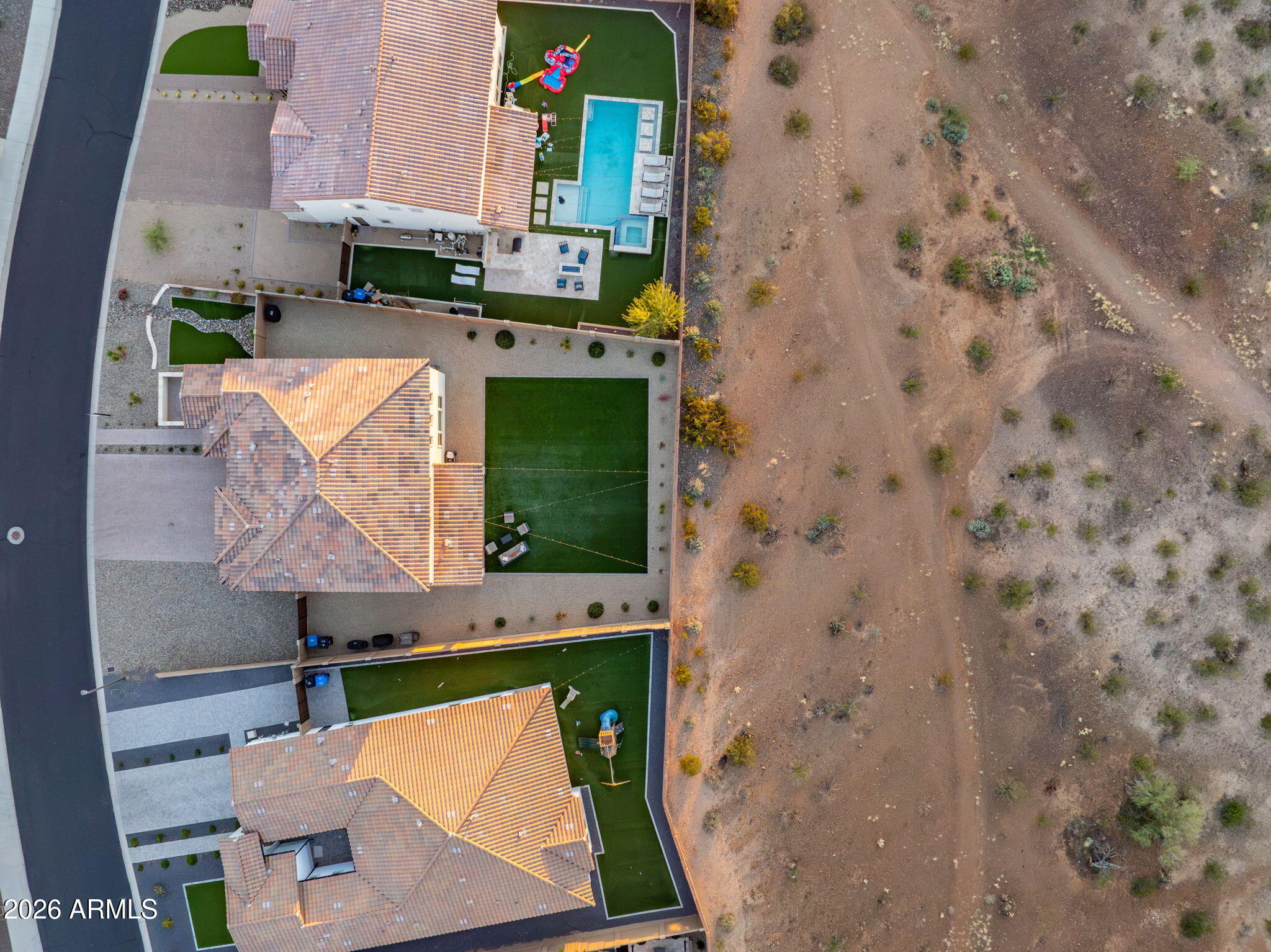 Aerial view of homes beside desert land, with a backyard pool and turf yards.