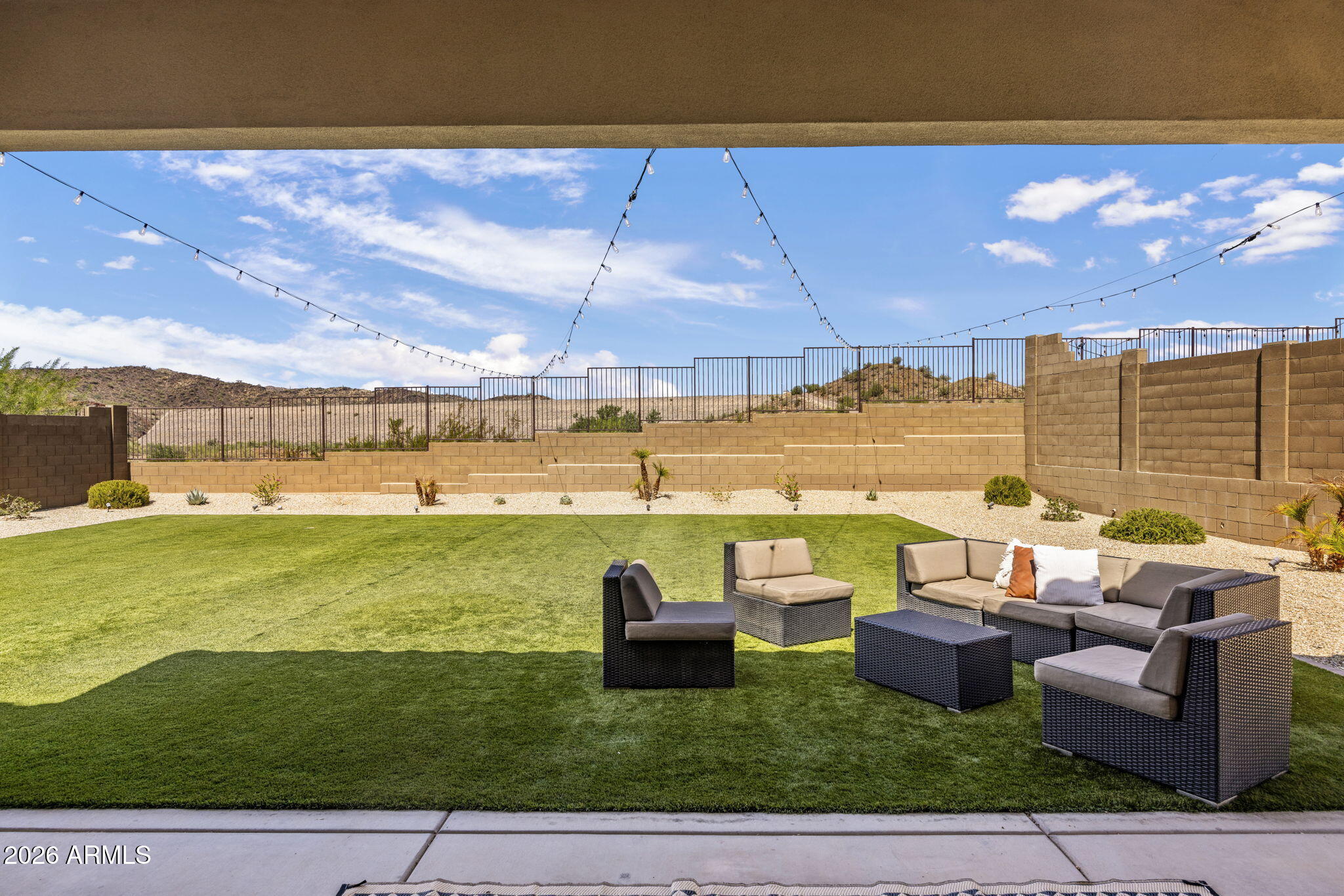 Backyard with artificial lawn, outdoor lounge seating, string lights, and desert hills beyond the fence.