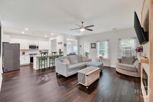 Open-concept living room and kitchen with a gray sectional, dark wood floors, and a bay-window seating nook.