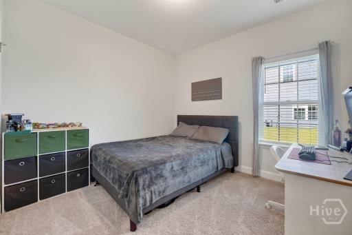 Furnished bedroom with a gray bed, green-and-black storage cubby, and desk by a curtained window.
