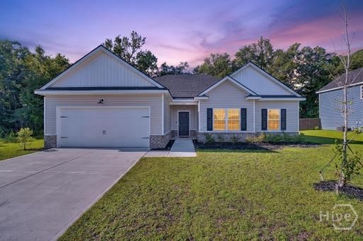 Single-story gray home with a two-car garage, lit windows, and a broad concrete driveway at dusk.