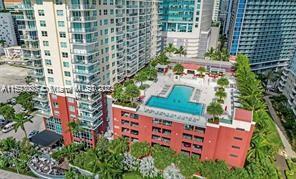Aerial view of a red condominium with a rooftop pool and landscaped terrace among taller towers.