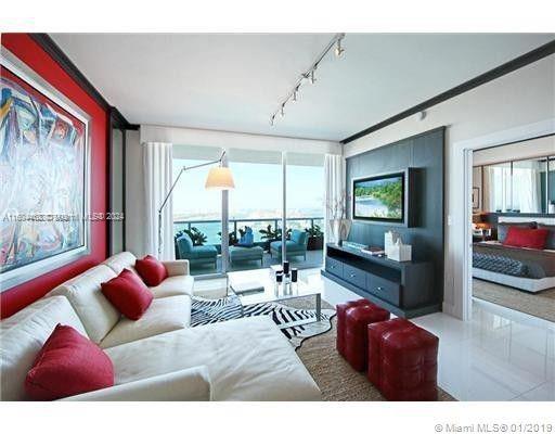 Living room with a white sectional, red accents, dark media wall, and balcony overlooking the water.