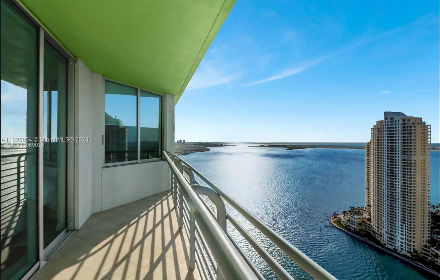 Condominium balcony overlooking blue water, with a neighboring high-rise tower along the shore.