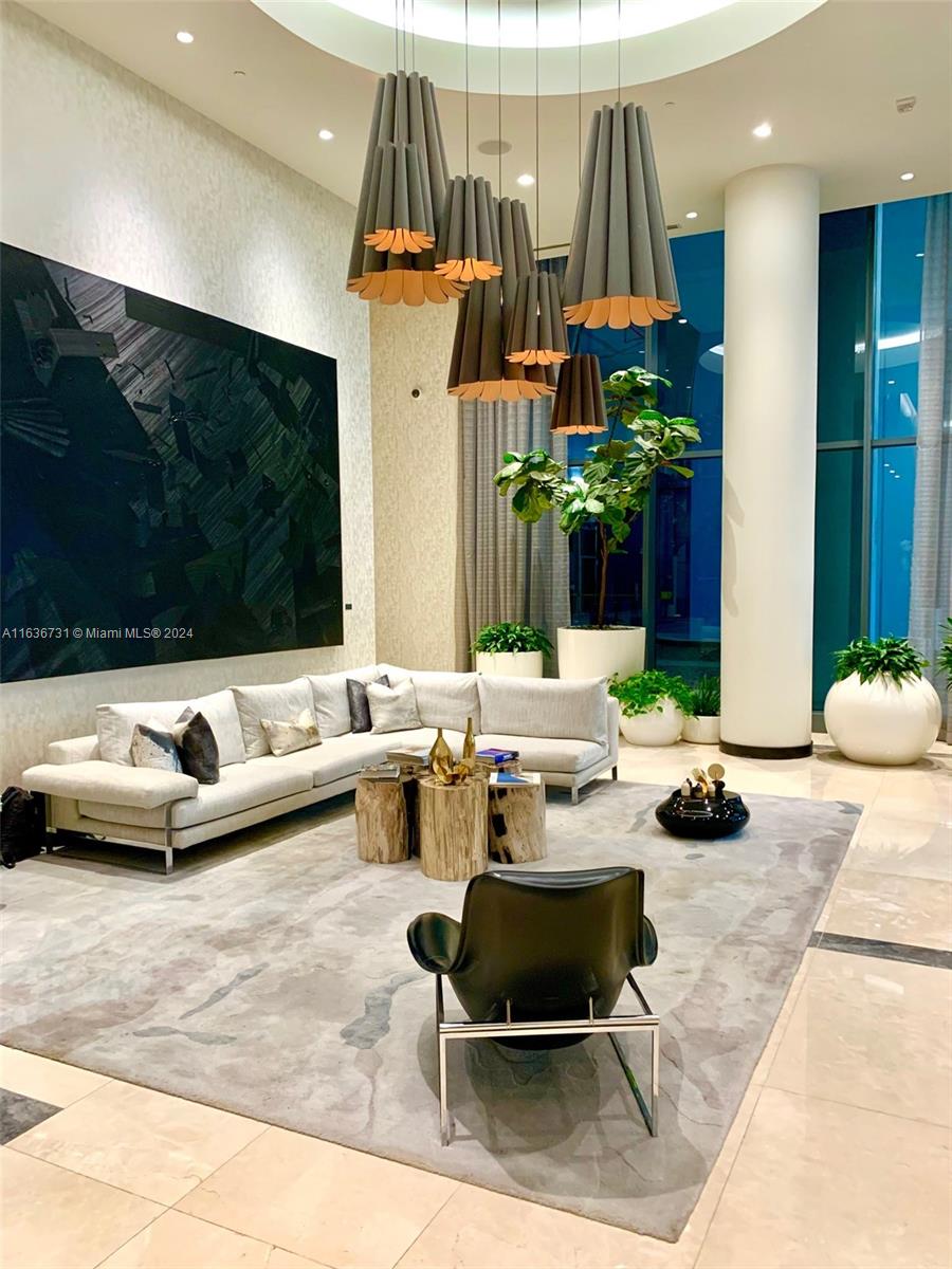Upscale lounge with a curved white sectional, sculptural pendant lights, and floor-to-ceiling blue windows.
